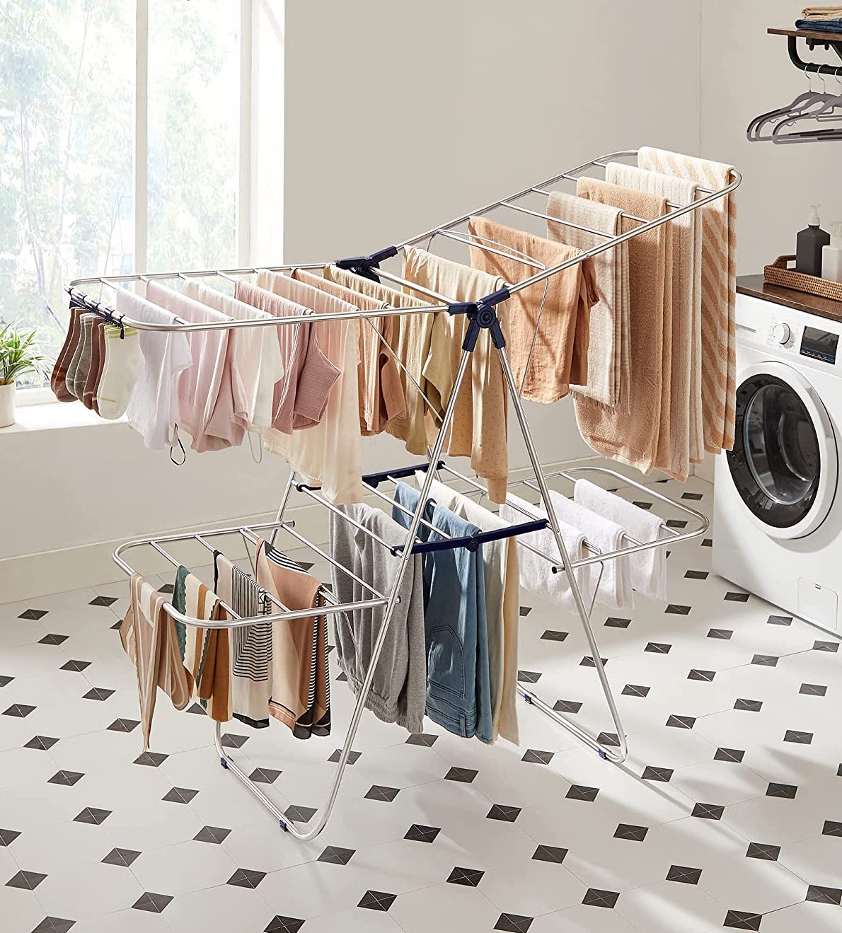 large drying rack on which several warm colored t shirts are hanging in a laundry room with black and white tiled floor