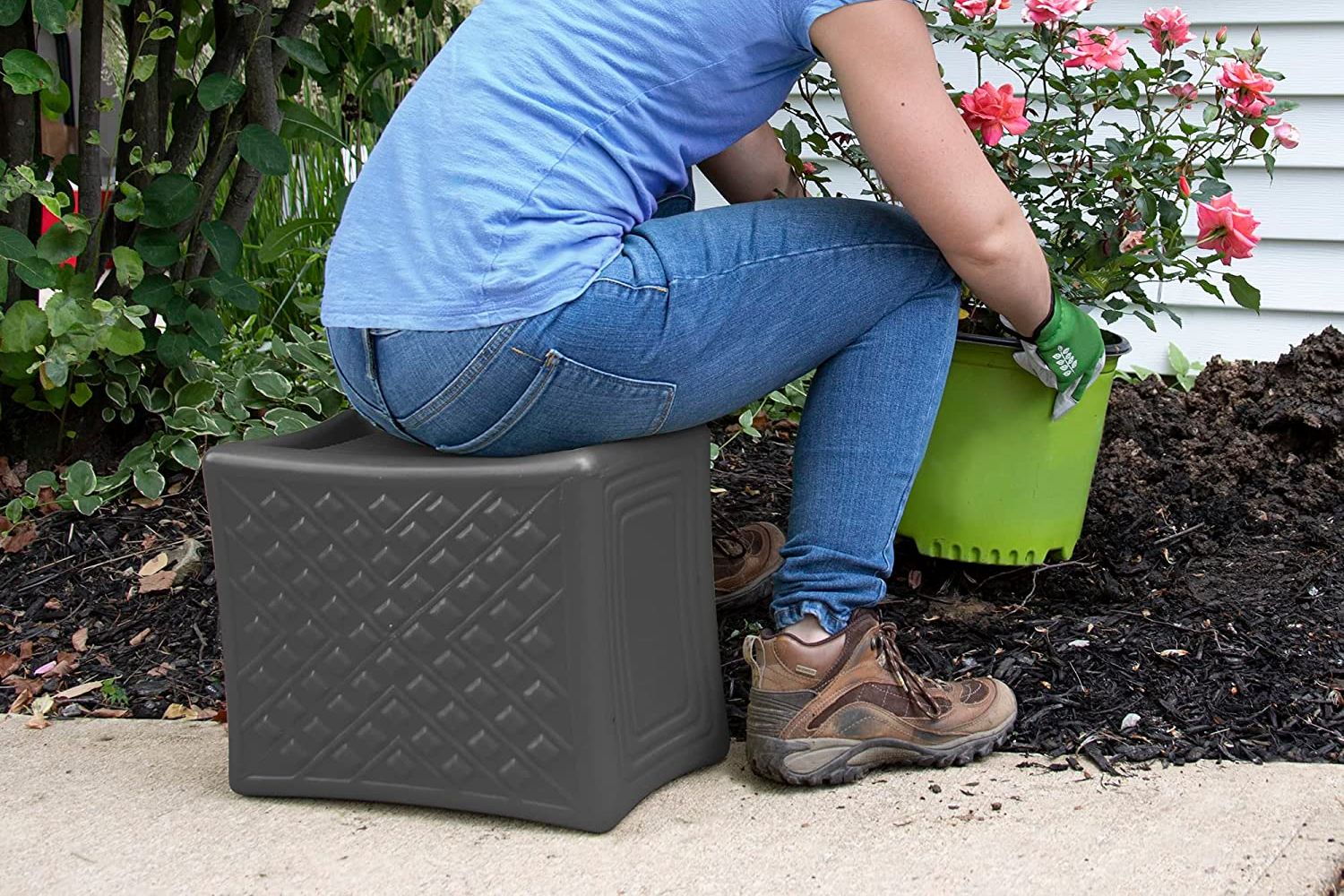 A person seated on the best gardening stool option while leaning over to pick up a large potted plant