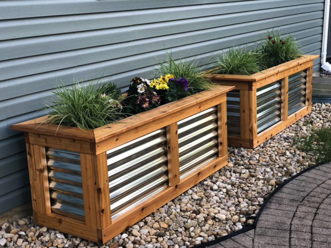 two large rectangular planter boxes with steel panels and purple and yellow flowers on side of house in rock landscaping