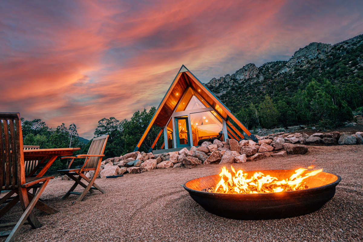 Burning fire pit on gravel lawn with A-frame house and stunning sunset in background