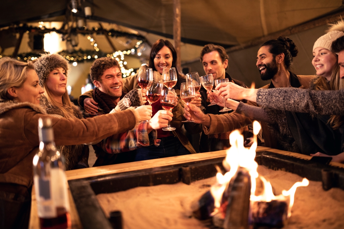 Group of people holding wine glasses around fire pit