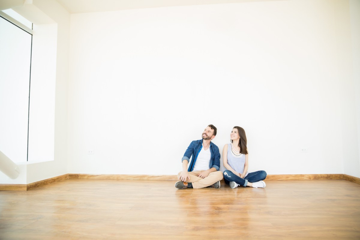 Owners Looking Away While Sitting On Floor In empty room of New Home