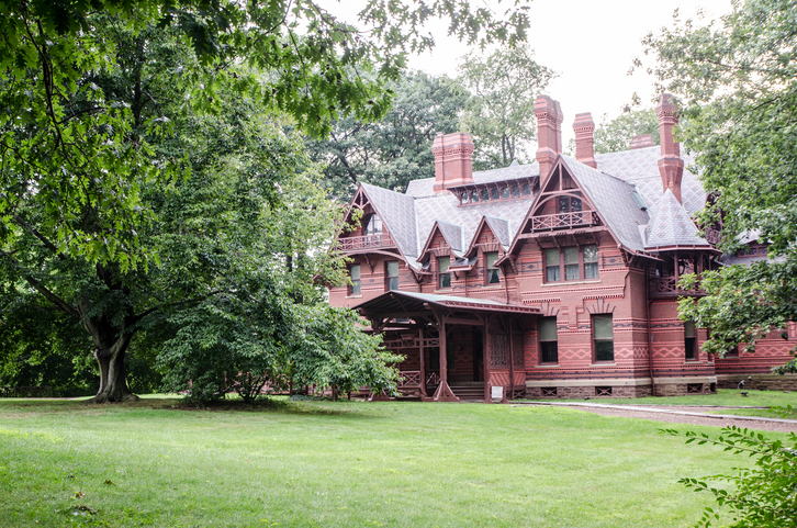 a-brick-red-High-Victorian-Gothic-house-on-a-spacious-green-lawn-with-large-trees
