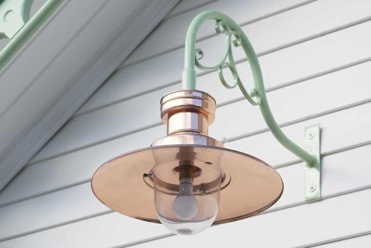 under-the-eave-of-a-white-house-there-is-a-copper-lamp-shade-handing-from-a-light-blue-ornamental-sconce