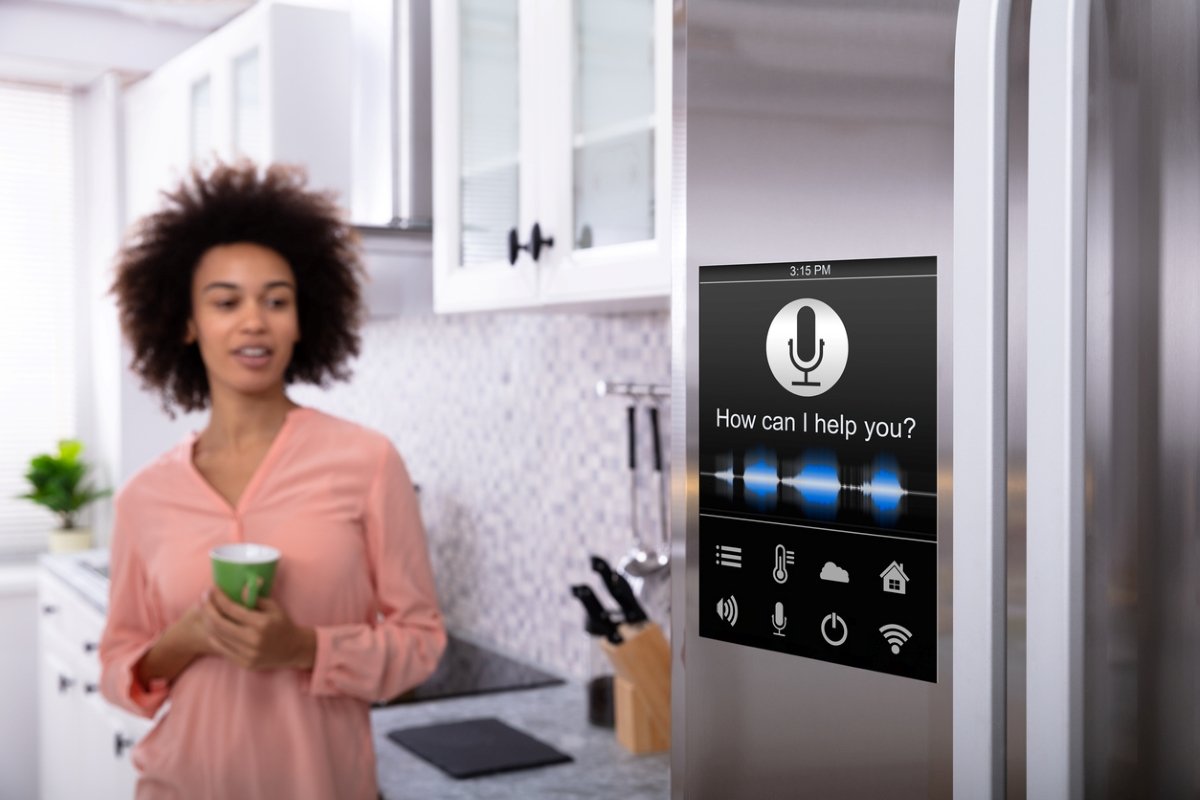 Smart fridge with the words, "How can I help you?" on a smart screen, a woman observing in the middle ground.