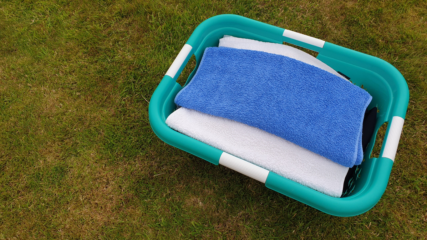 blue and white towels folded inside green laundry basket sitting outside on green grass