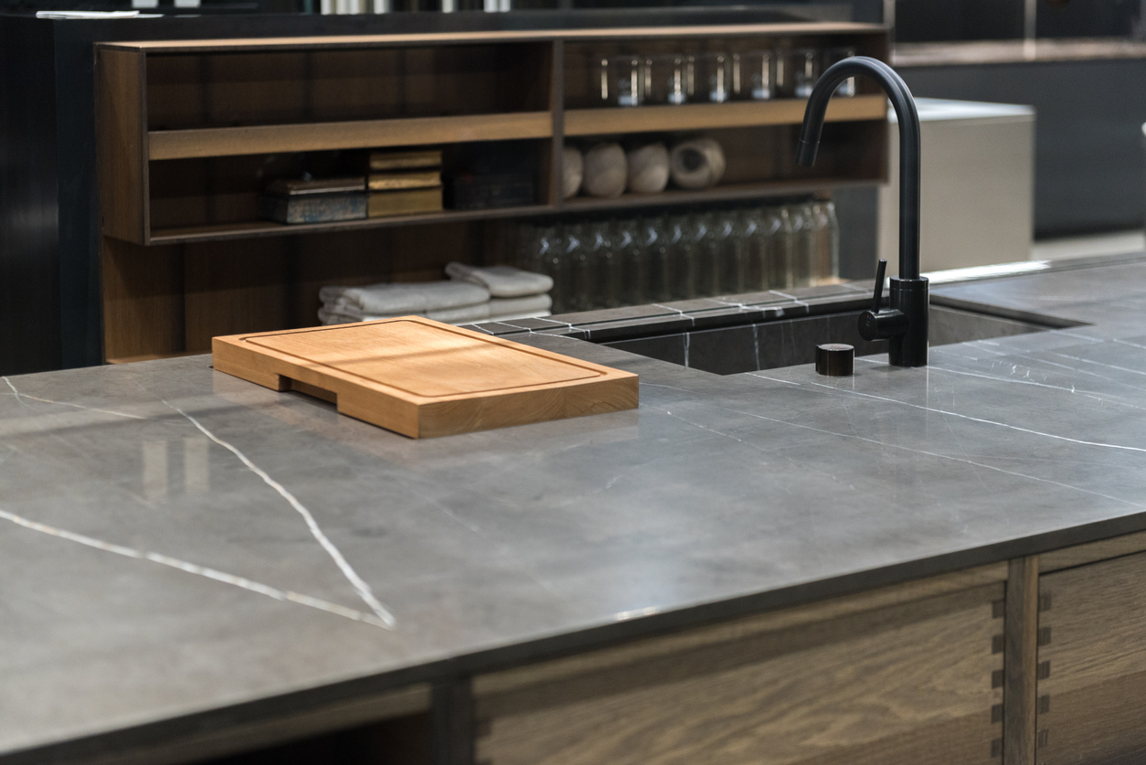 dark grey soapstone countertop island with sink and wooden cutting board in grey colored kitchen