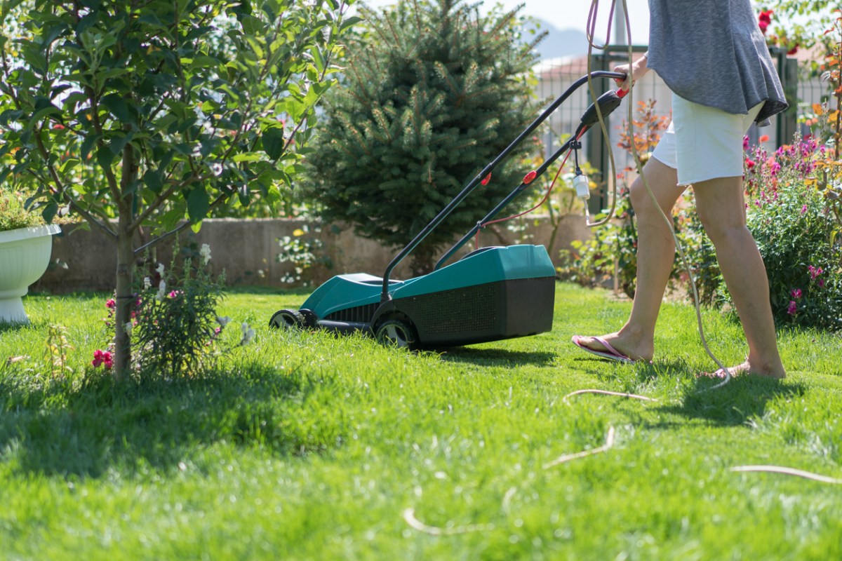 Woman mowing the lawn, lawnmower with cable.