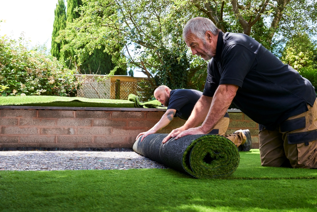 Men rolling out artificial turf in a yard.