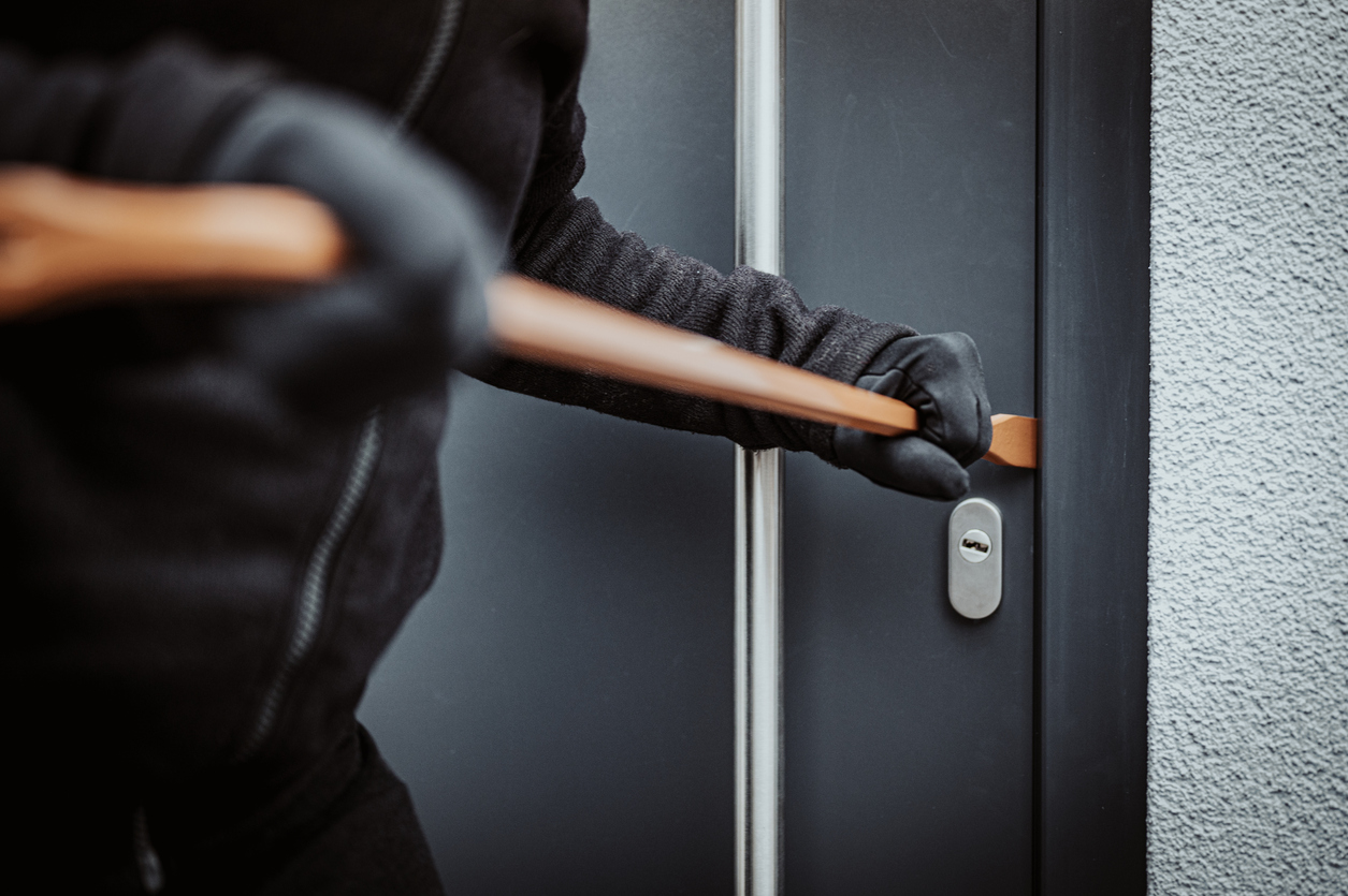 Burglar trying to break into a black steel door with a crow bar.