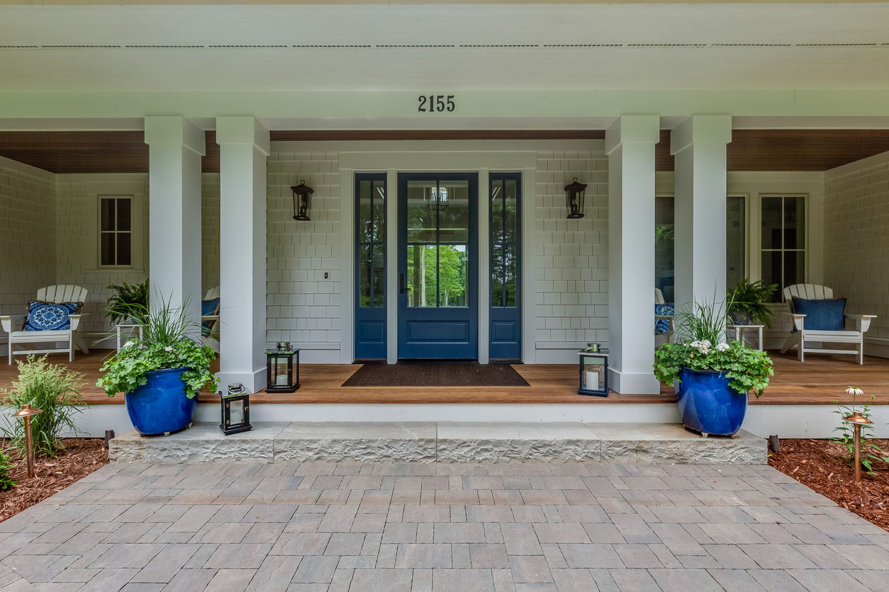 large elegant front porch on white house with blue door and blue flower pot and pillow accents