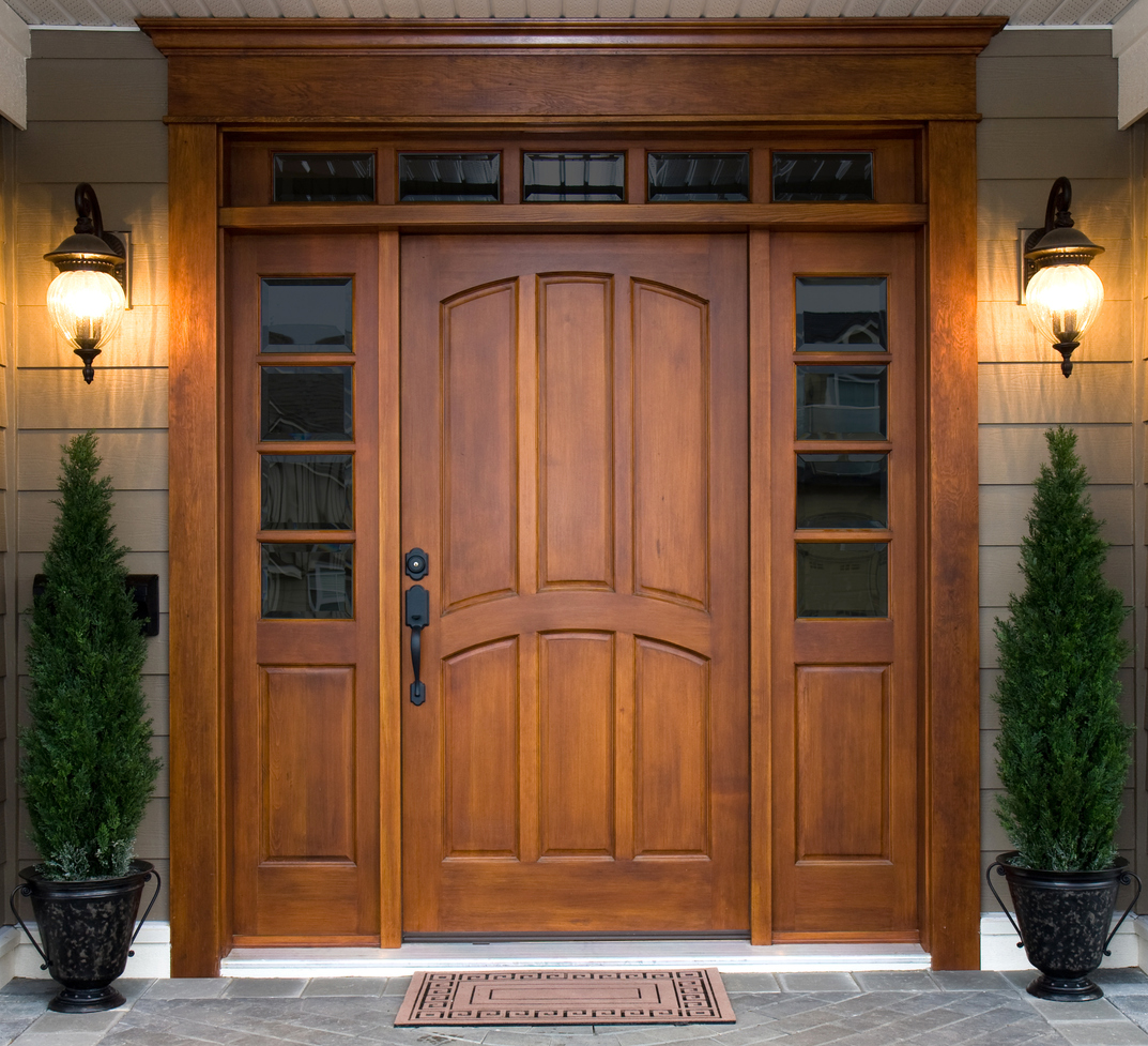 beautiful front door made of dark wood flanked by two house lights on front porch