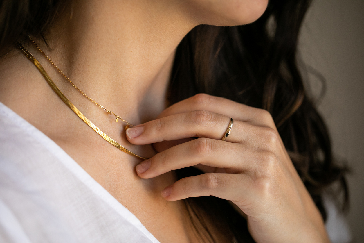 close up on neck of brunette woman in white t-shirt wearing a gold necklace and a ring on one hand