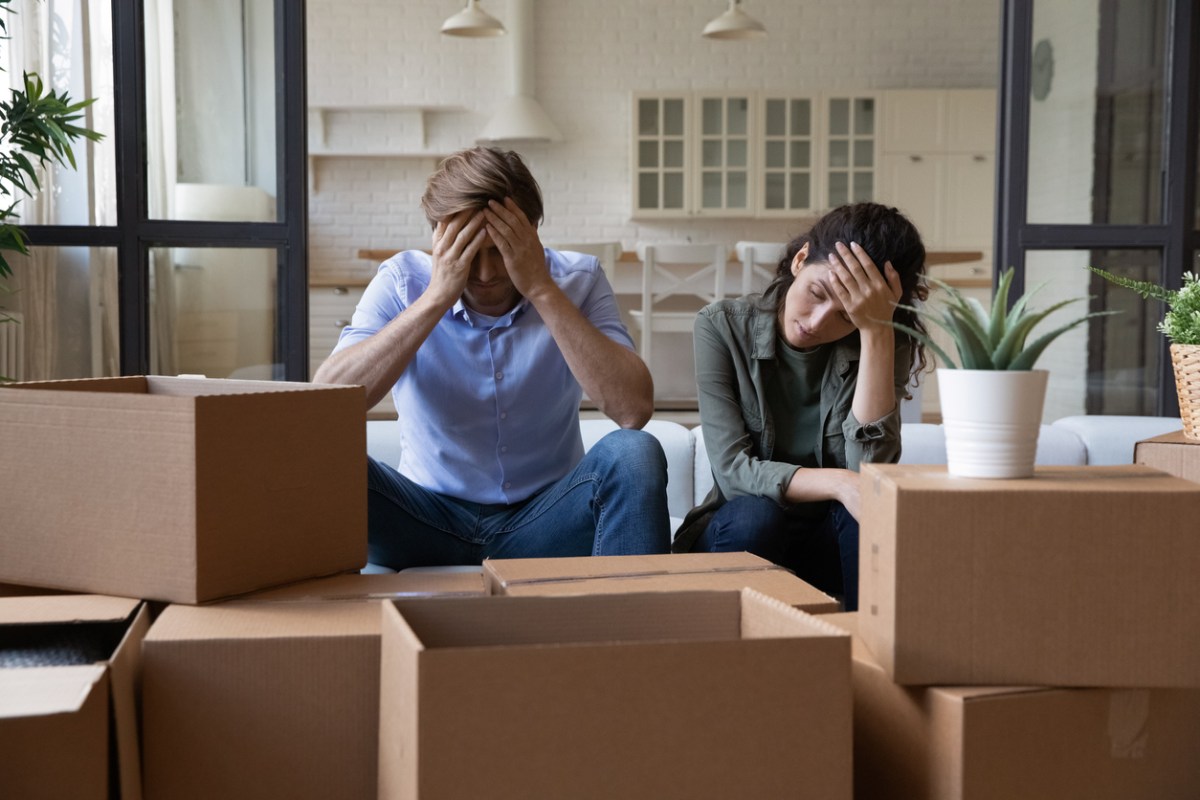 Exhausted couple sit near cardboard boxes at relocation day