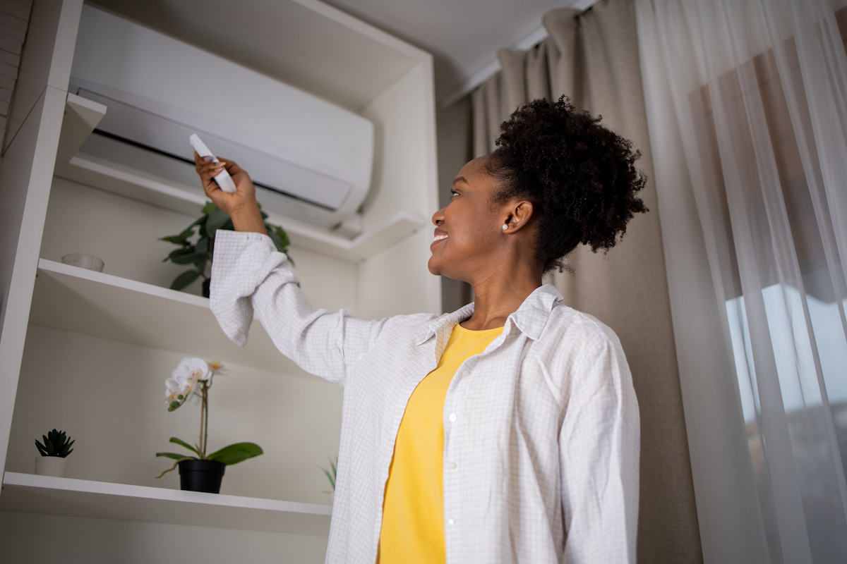 woman turning on a mini-split air conditioning unit with a remote