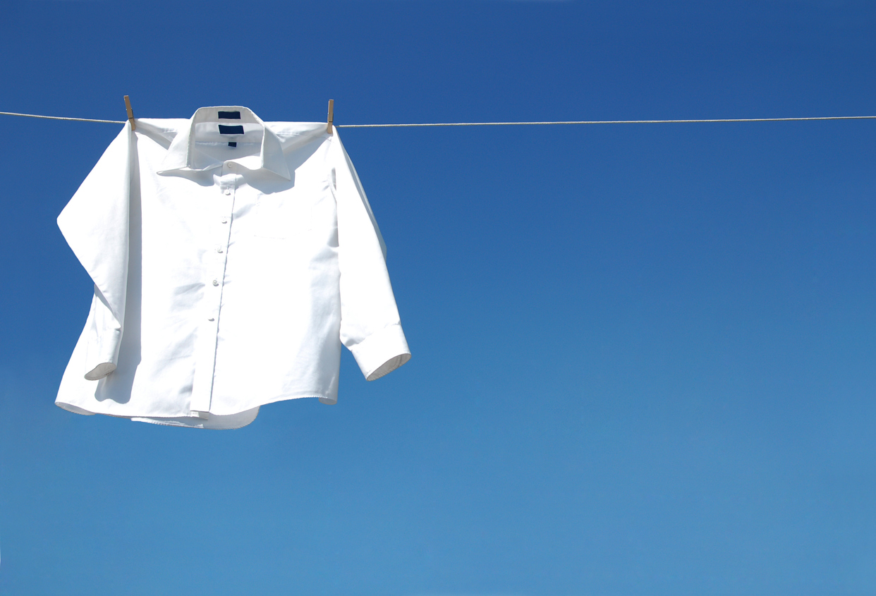 a single crisp white blouse hanging on clothes line in front of bright blue sky