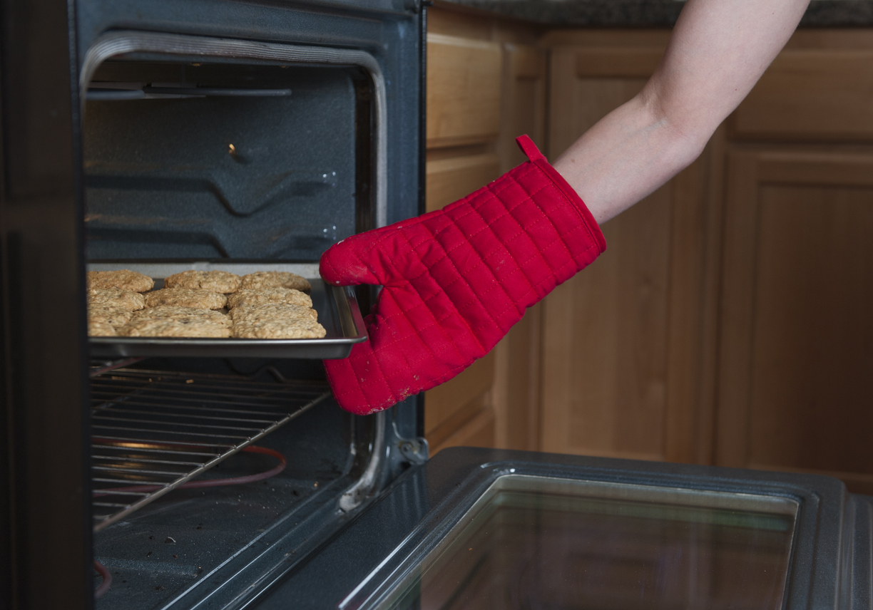 woman's hand wearing red oven mitt pulling cookies out of oven