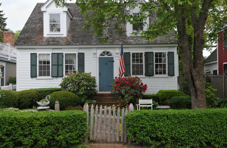 white-cottage-style.-house-with-landscaping-and.an-American-flag-and-a-hedge-for-the-front-fence