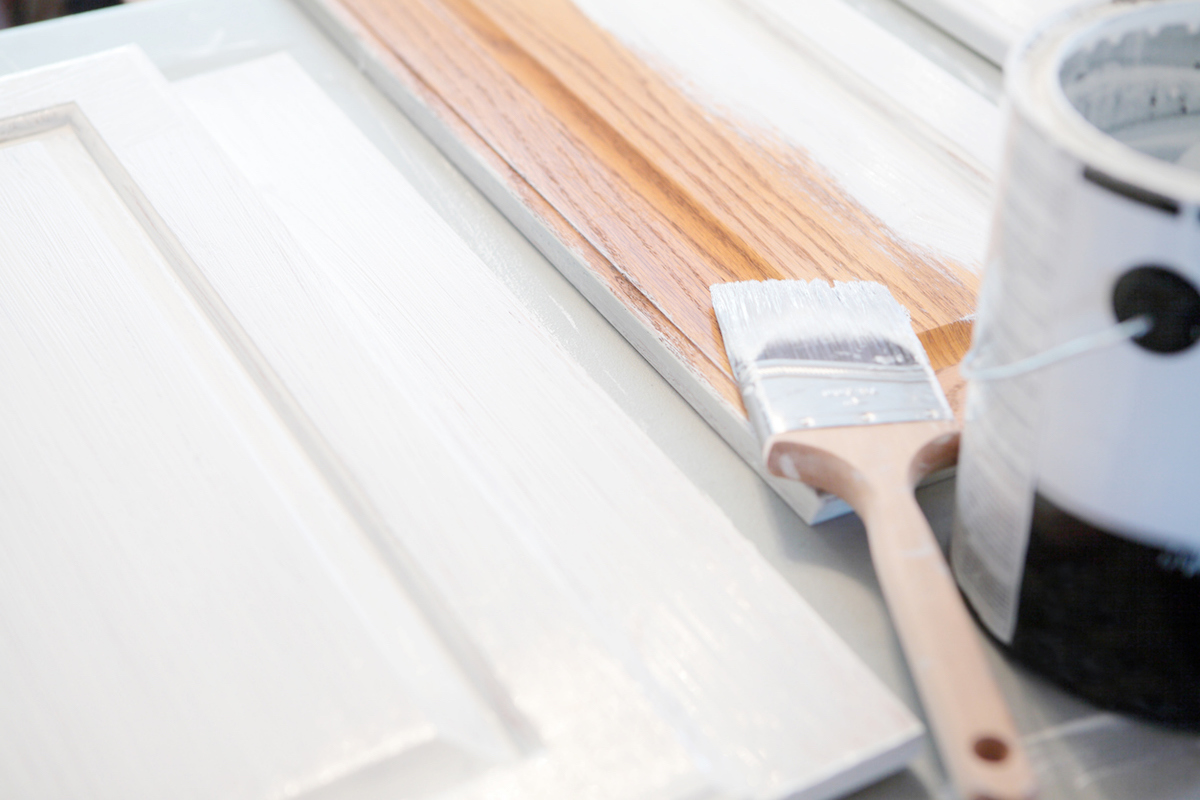 low voc white paint on wood cabinets with wet paintbrush and can of paint