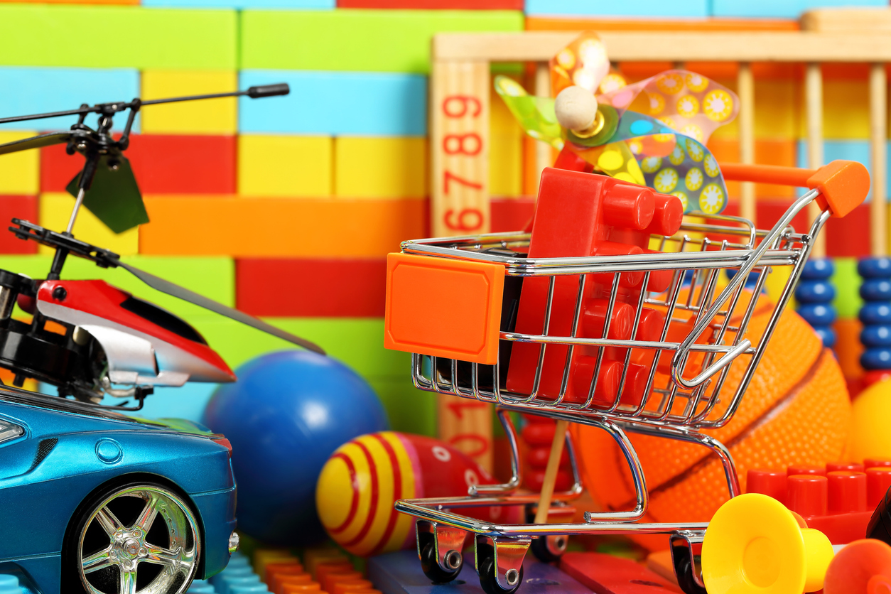 close up on small toys a mini shopping cart with a red lego inside a toy car and toy helicopter in front of a wall of colorful blocks