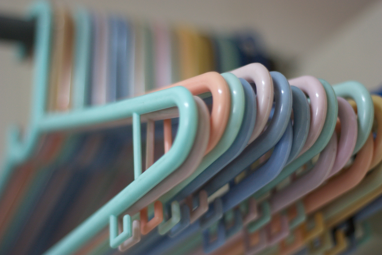 close up on pastel colored plastic hangers hanging in closet