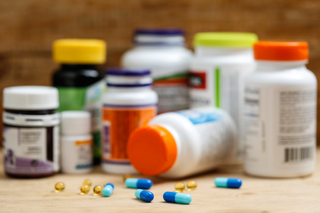 bottles of medicine and vitamins in blurry focus on countertop with blue prescription pills on counter