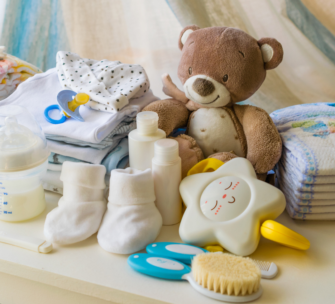 baby products on top of white dresser including brown teddy bear, pacifier, star shaped toy, baby shoes and baby bottle