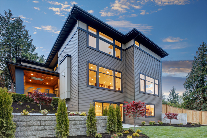 contemporary-house-with-three-stories-and-a-pale-blue-paint-scheme-and-landscaping-against-sunset-sky