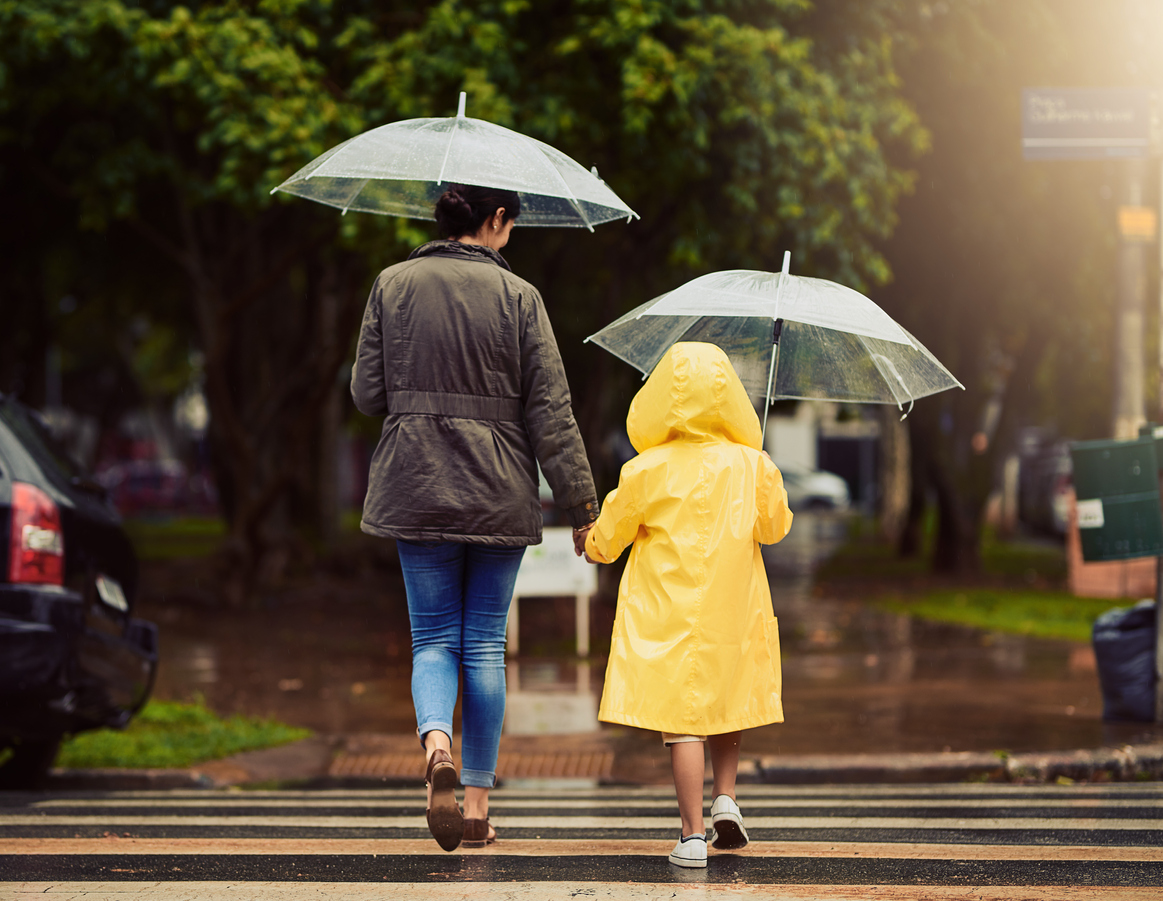 mother and daughter in yellow rain coat crossing the street both holding clear umbrellas