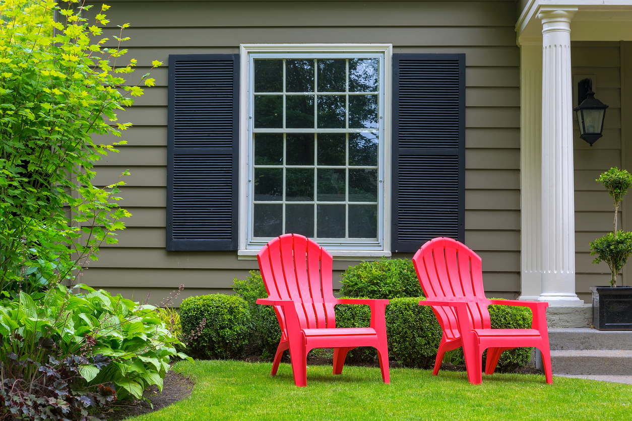 two red adirondack chairs in front law of grey house