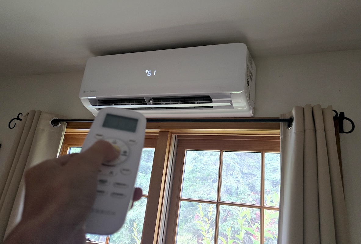 Person holds a remote control in front of a mini-split unit above a window.