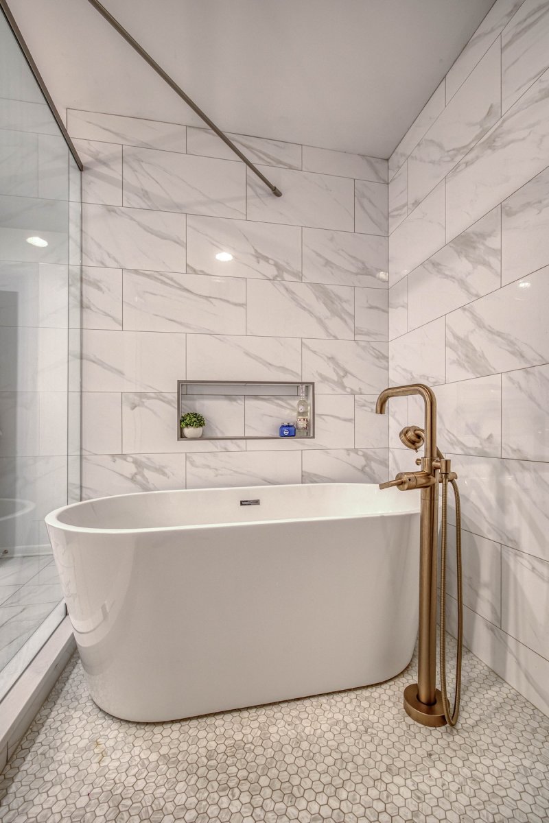 Freestanding white tub in a bathroom with marble walls and penny tiles on the floors.