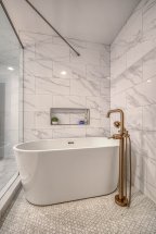 Freestanding white tub in a bathroom with marble walls and penny tiles on the floors.