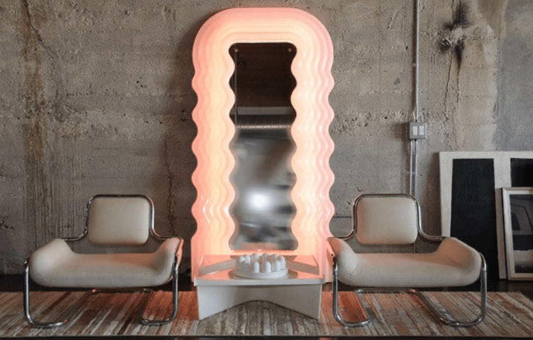 industrial looking sitting room with two white chairs flanking a large full length mirror with a bright pink frame
