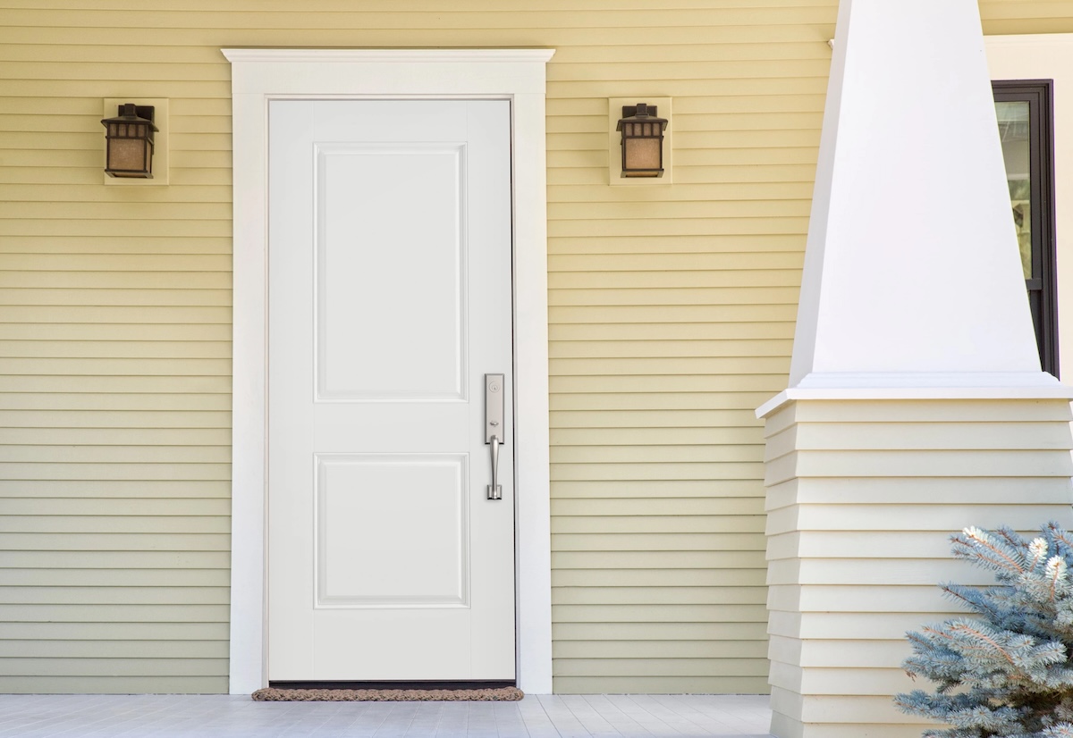 A white front door with brushed silver hardware on a beige-yellow house with an obelisk-shaped pillar to the right.