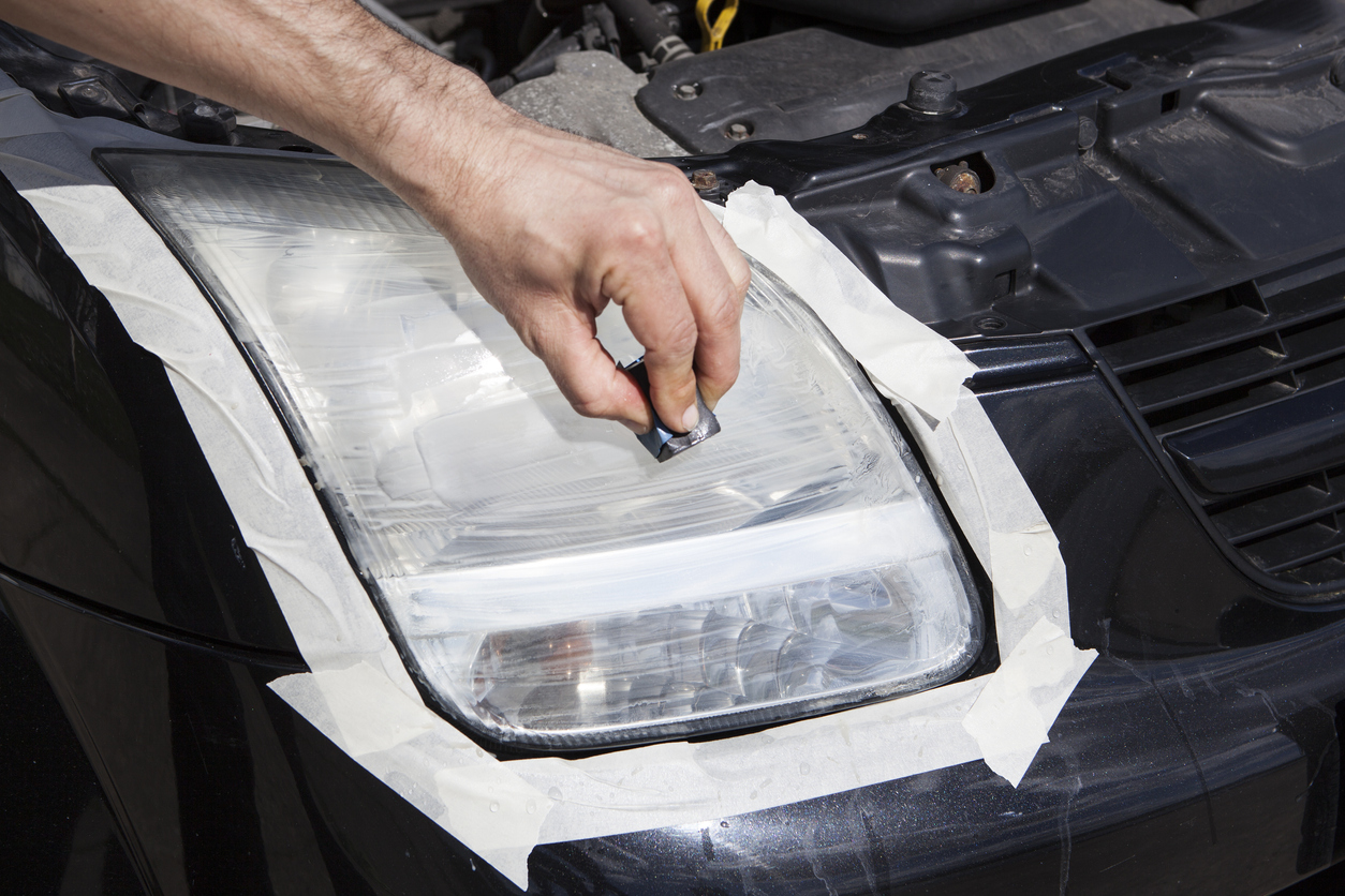 Hand applying headlight kit materials to a black car's passenger headlight
