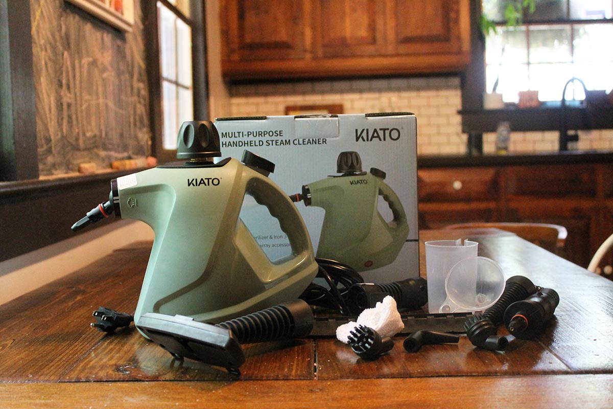 The Kiato handheld steam cleaner next to its box and all included accessories