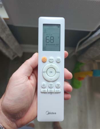 A close-up of a hand holding the remote control for the Midea U-shaped air conditioner