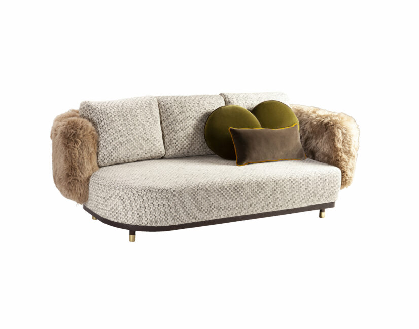 a tan sofa with rounded edges and a faux fur texture on arms with two velvet pillows
