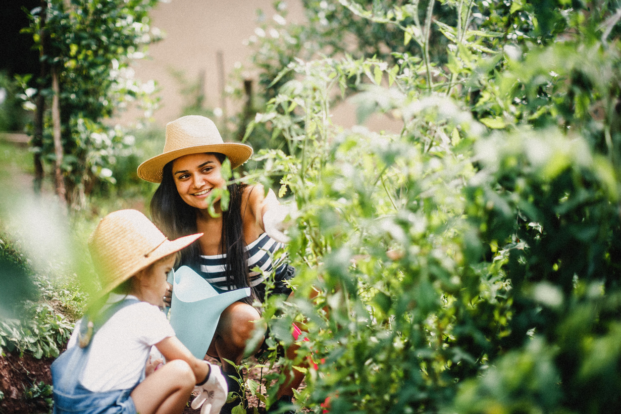 A woman and child wearing the best gardening hats options while kneeling next to a large outdoor plant
