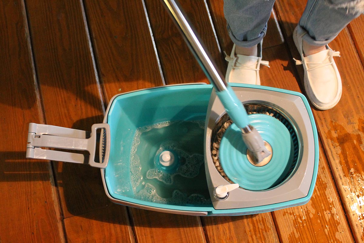 Person wringing aqua spin mop in bucket