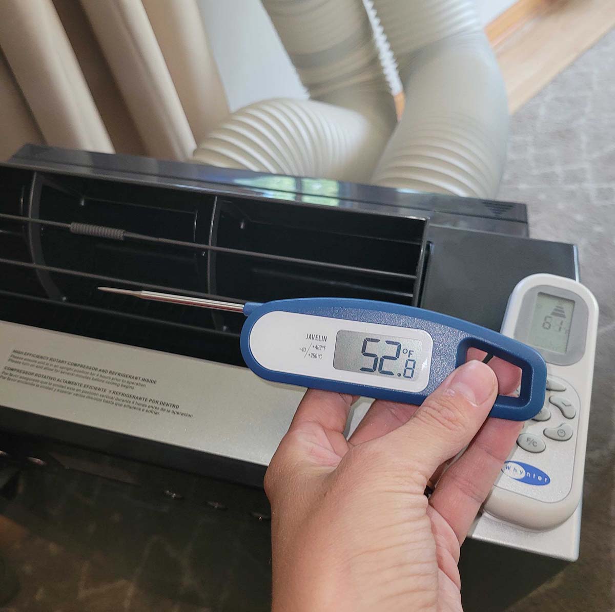A person holding a digital thermometer next to Whynter Portable Air Conditioner