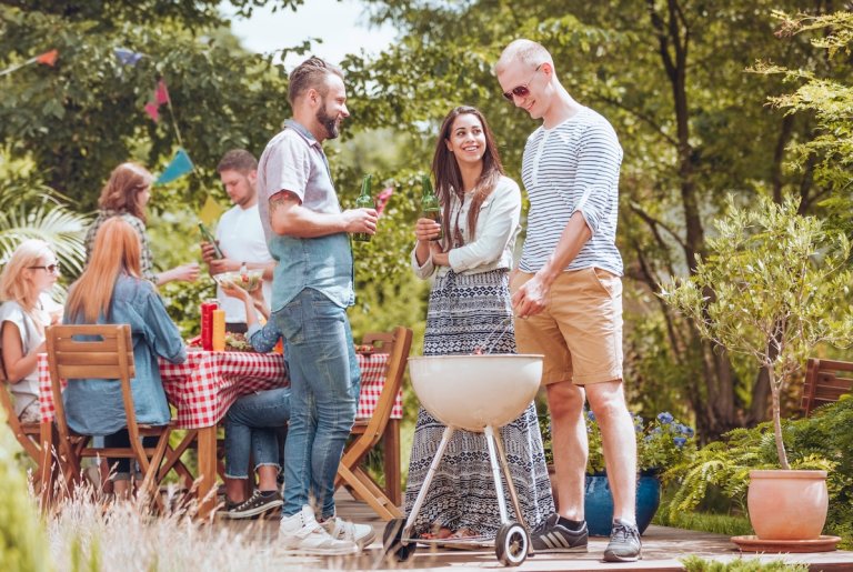 Group of seven young people eating outside with a grill and a picnic table on a patio area.