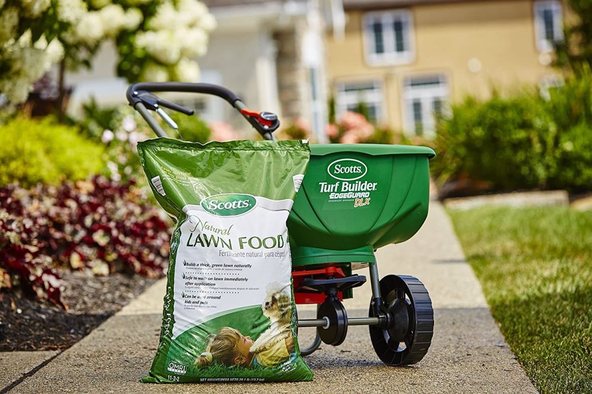 The best lawn fertilizer for spring option sits in its bag on a sidewalk next to a fertilizer spreader