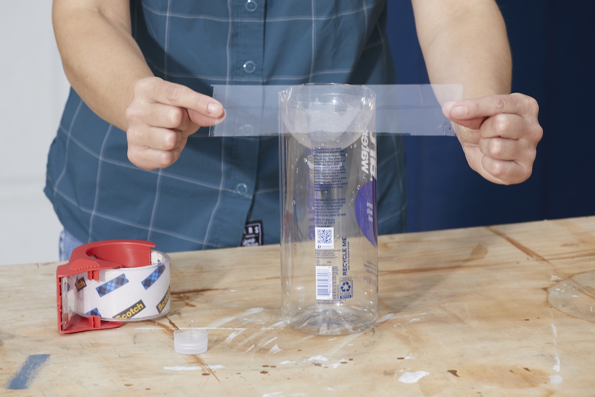 Woman tapes the inverted cut top of a soda bottle into the bottom of the bottle to make a bug trap.