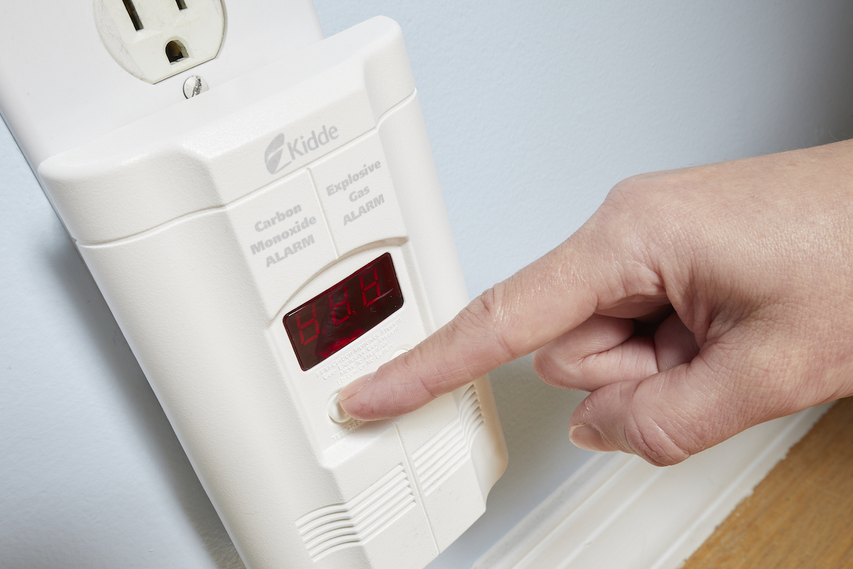 Woman presses the "test" button on a carbon monoxide detector.