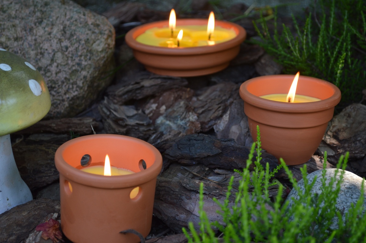 Three lit citronella candles in terracotta candle holders.