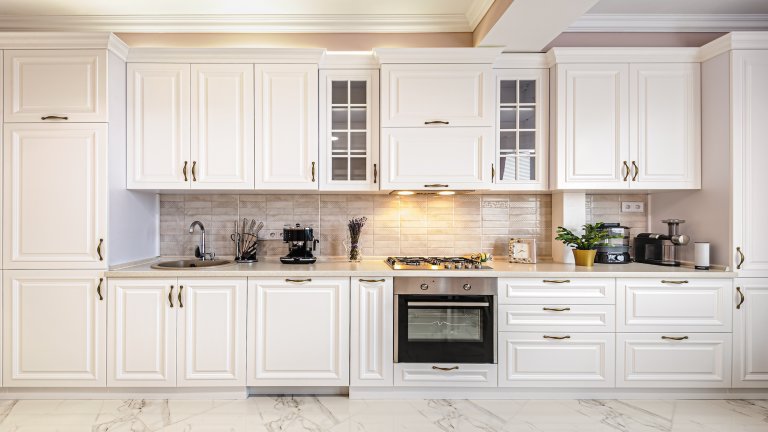 A simple, white kitchen with a pantry cabinets, drawer cabinets, and windowed cabinets.