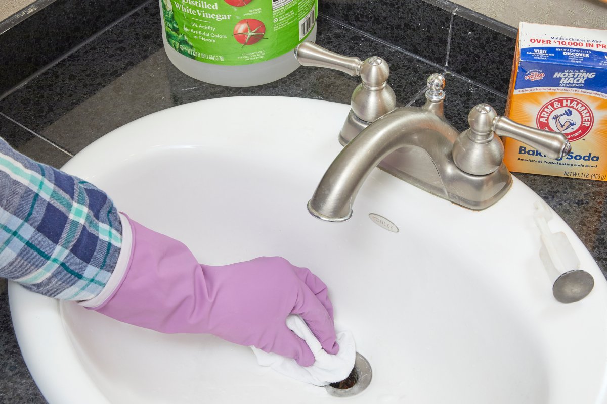 Woman puts baking soda and vinegar down a bathroom sink drain.