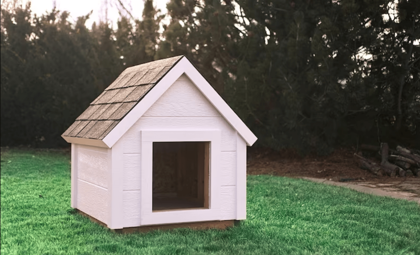 classic dog house with triangular roof made with white wood in backyard with green grass